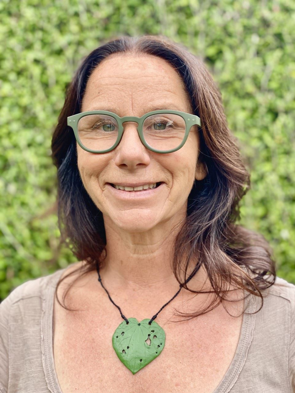 Presenter Sam wearing green glasses and green necklace in front of greenery background
